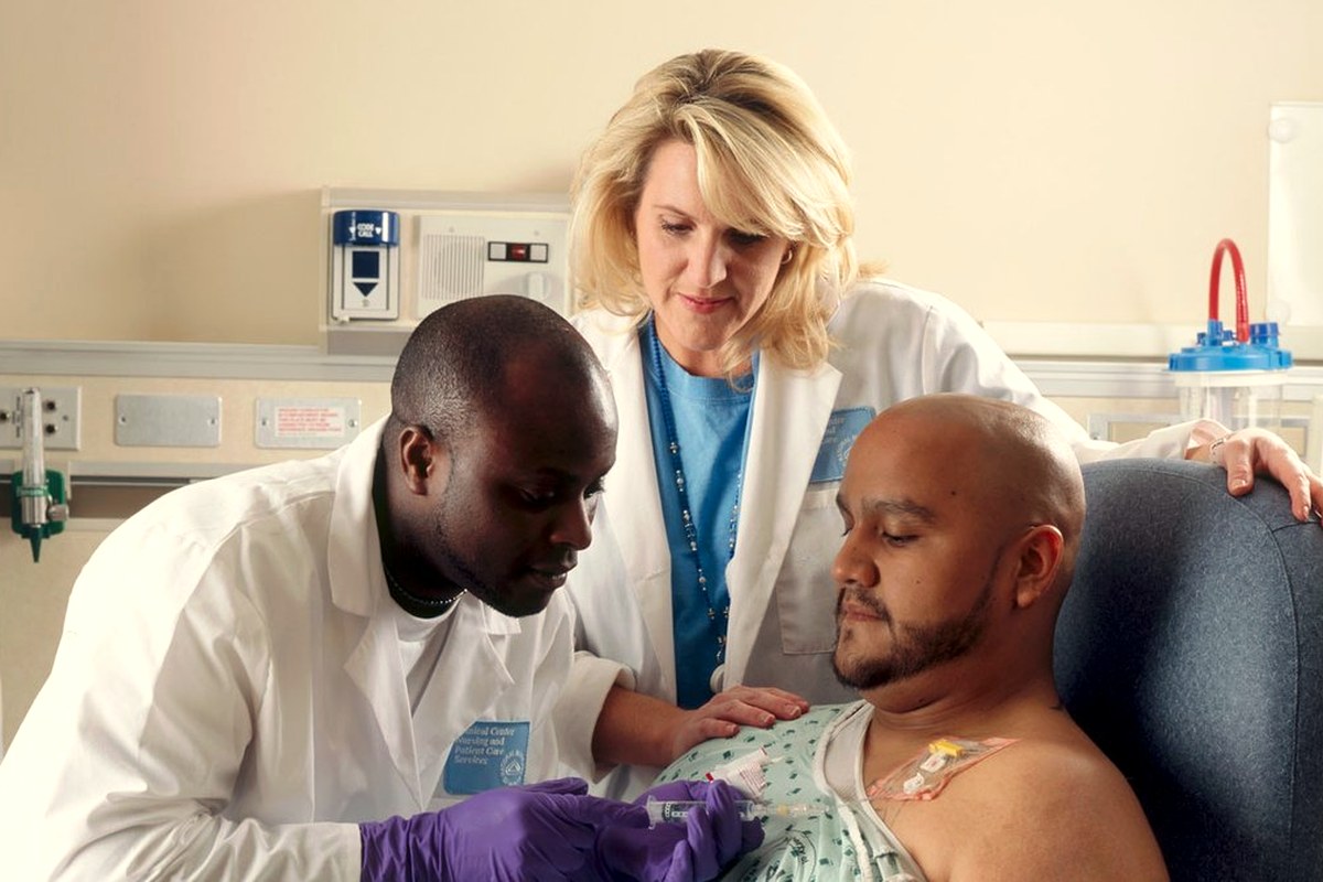 A patient receiving chemotherapy through a chest port while two clinicians attend